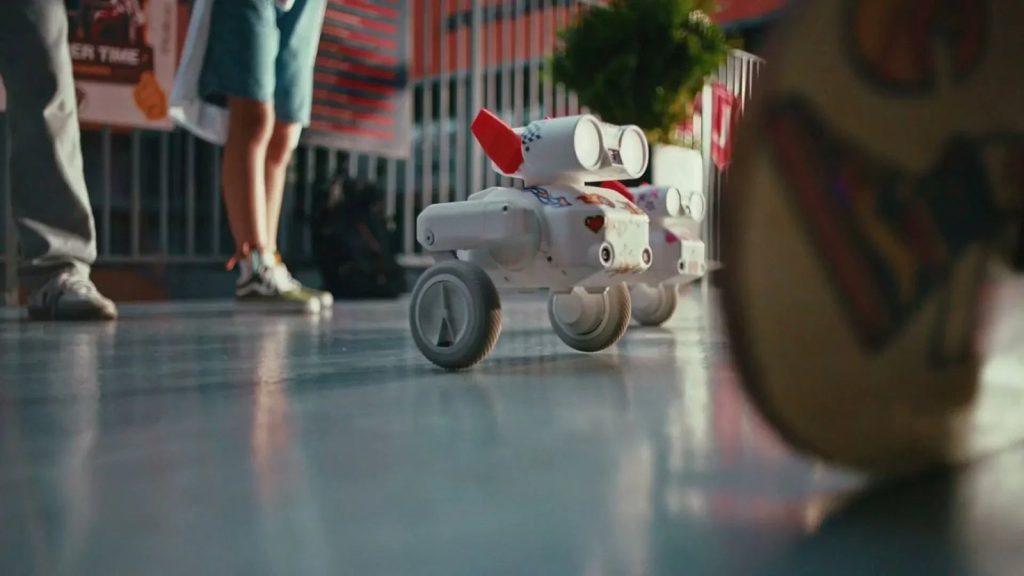 Two Beni all-terrain follow-cam camera robots standing indoors on a wooden floor next to a charging dock